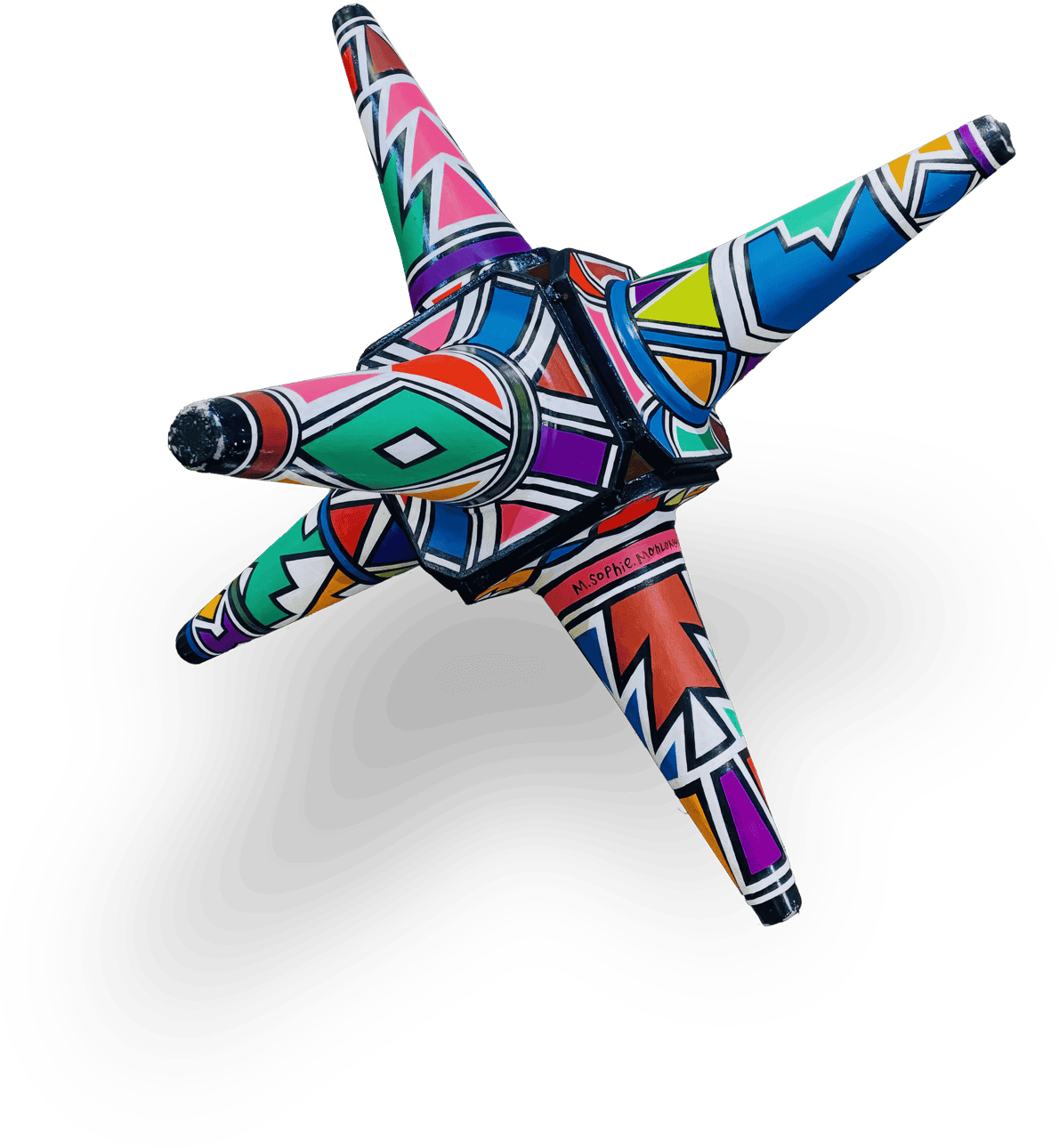 A colourful, geometric star-shaped sculpture with five pointed arms, each decorated in bold, intricate patterns of red, blue, green, orange, yellow, purple, black and white. The patterns feature zigzags and diamonds. The background is transparent.