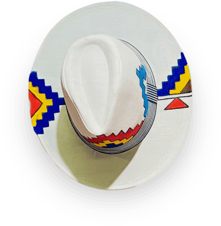 A white hat with a wide brim features bold, colourful geometric patterns in red, blue, yellow, and black, resembling traditional indigenous or folk art. The hat is photographed from above on a black background.