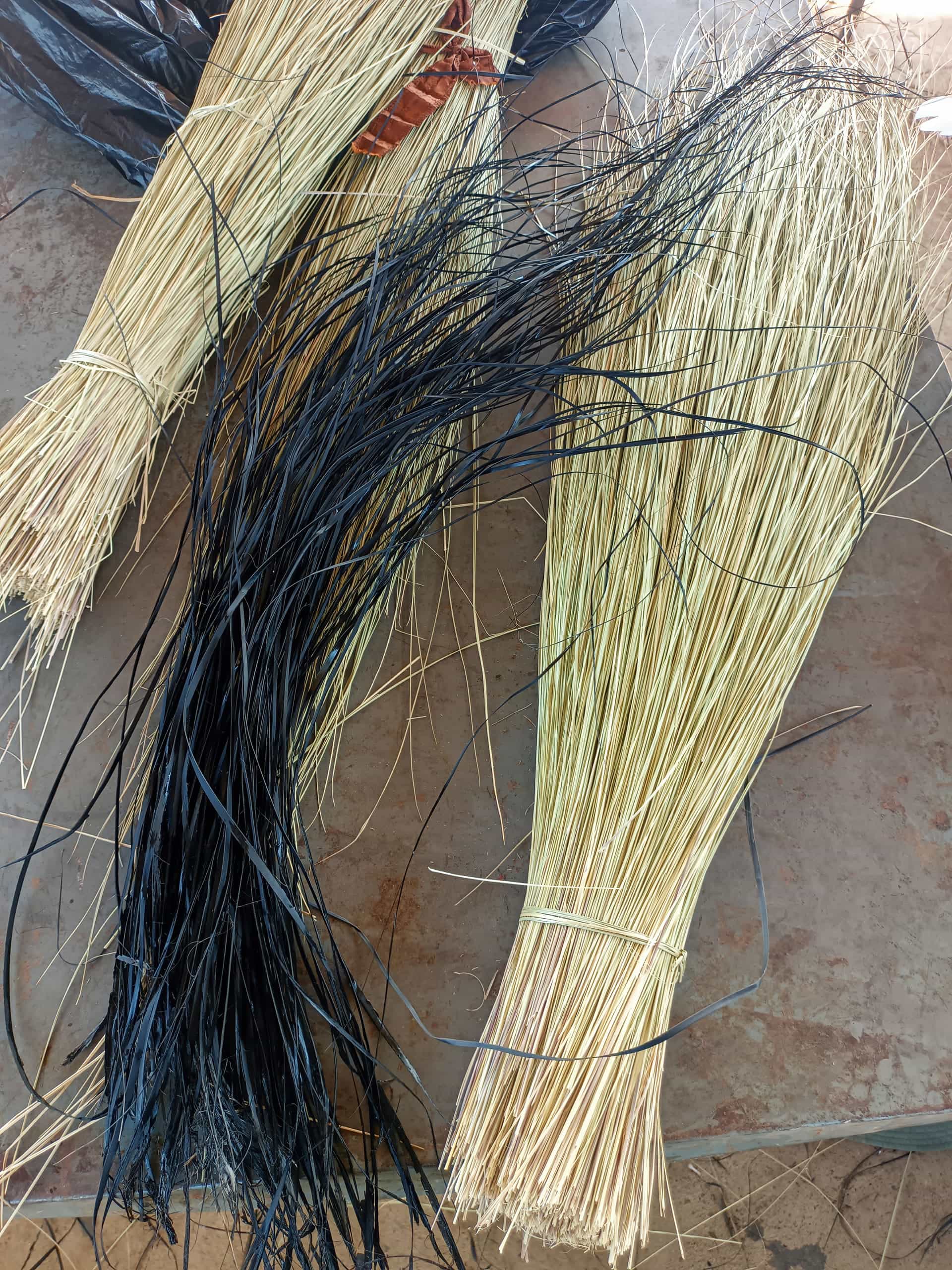 Bundles of long, thin, dried grass or reeds lie on a stone surface. Two light tan bundles are tied with string, while a third bundle is dyed black. The strands are neatly grouped but splay out at the ends, showing varied textures.