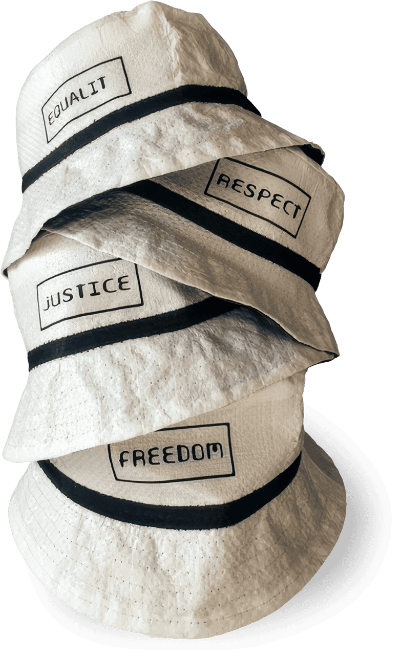 Four white bucket hats with black bands are stacked vertically. Each hat has a different word in black capital letters within a rectangle: “EQUALITY”, “RESPECT”, “JUSTICE”, and “FREEDOM”. The background is black.