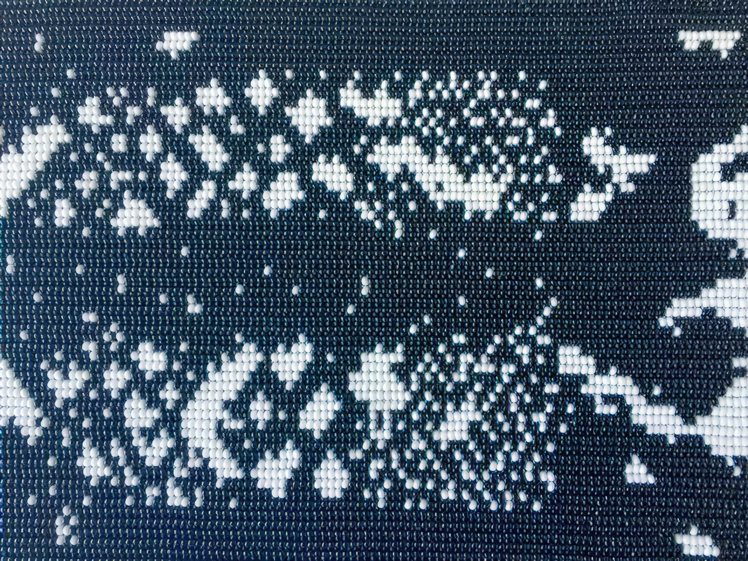 Close-up of a mosaic made from small, round, shiny beads arranged on a grid. The beads form an abstract black and white pattern with scattered clusters that create a high-contrast, pixelated effect, resembling a digital image or code.