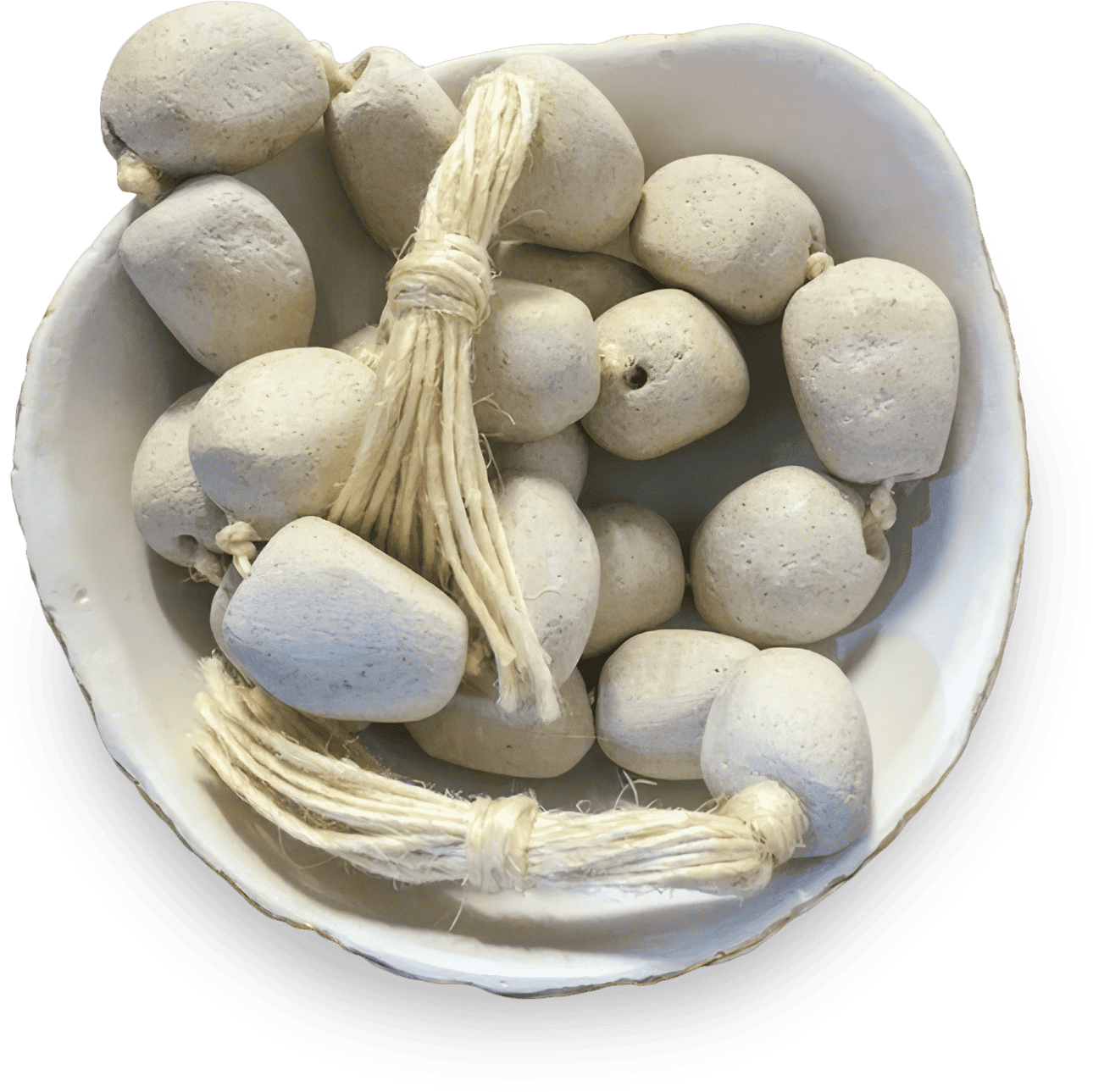A white bowl contains several smooth, pale grey stone beads. Some beads are strung together with natural, thick, tan twine tied in knots, while others are loose. The bowl and beads have a handmade, rustic appearance.