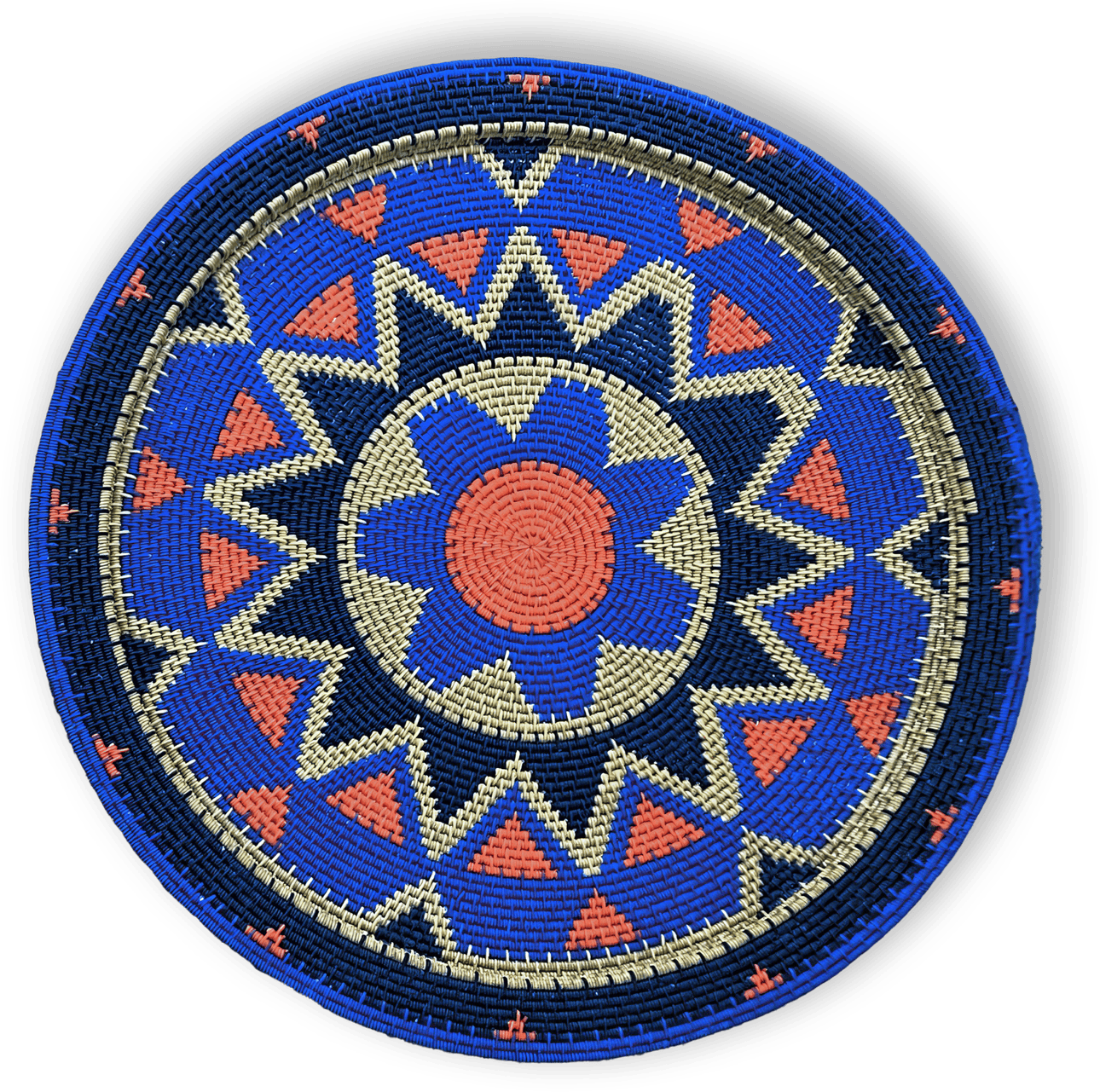 A round, woven basket lid features a geometric pattern in blue, coral orange, cream, and navy. The design includes a central flower-like shape, surrounded by alternating triangles and zigzag bands, creating a vibrant, symmetrical motif.