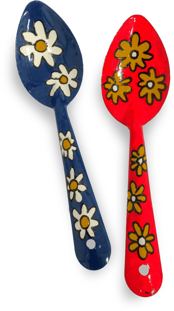 Two colourful spoons are shown. One is blue with white daisy flowers and yellow centres, while the other is red with yellow and white daisies. Both handles have holes at the base for hanging and are decorated with matching floral patterns.