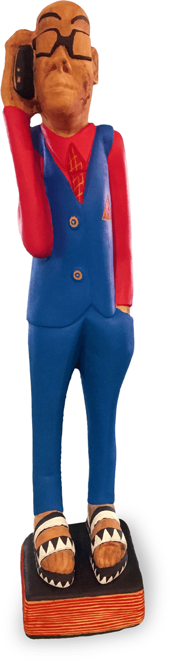 A colourful wooden sculpture of a person in a blue suit, red shirt, and tie, wearing glasses, holding a black phone to their ear, and standing on a striped base with patterned shoes. The figure has exaggerated facial features and a stylised appearance.