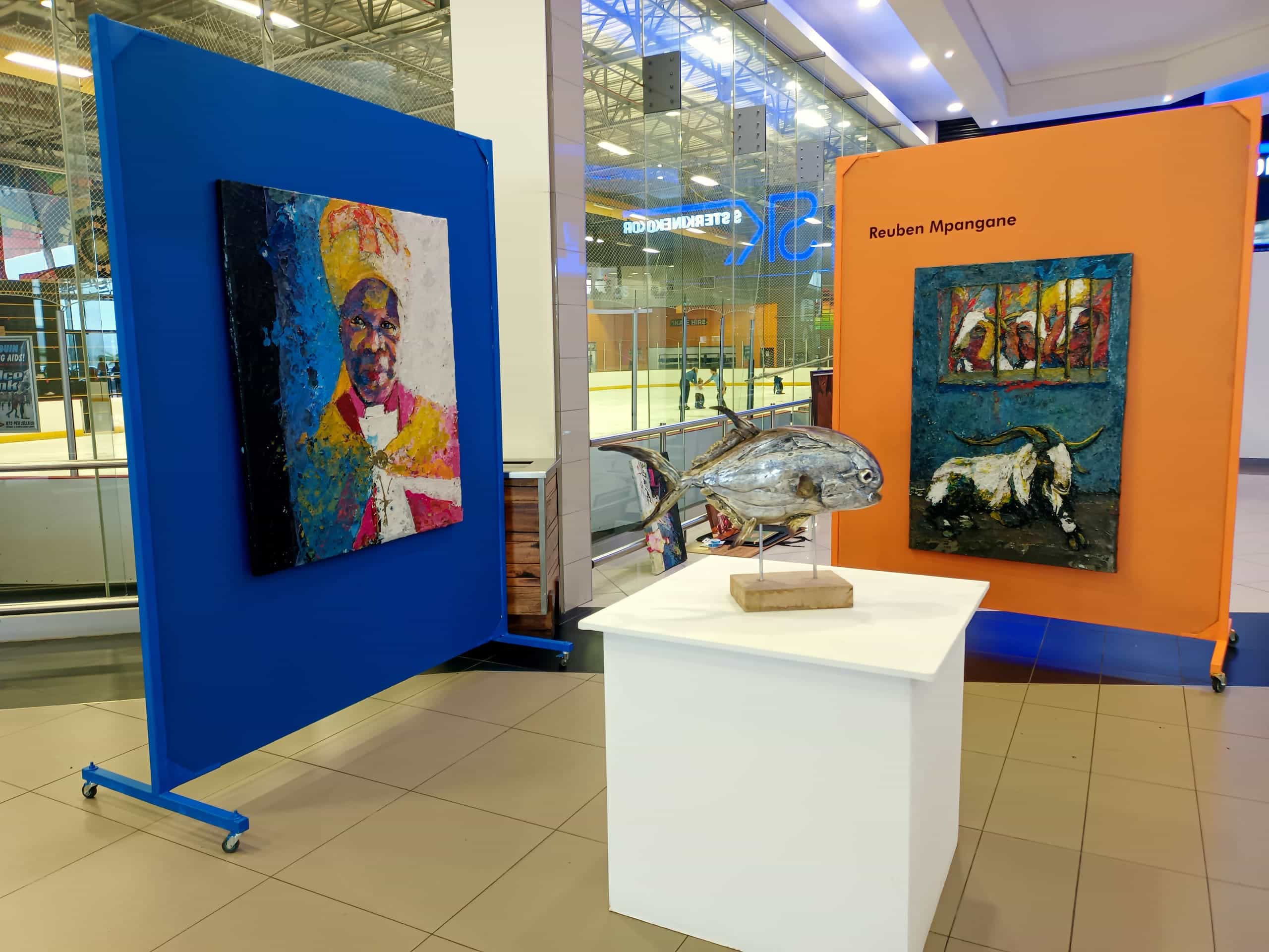 Two colourful art panels are displayed in a shopping centre, one blue with a textured portrait and one orange labelled 