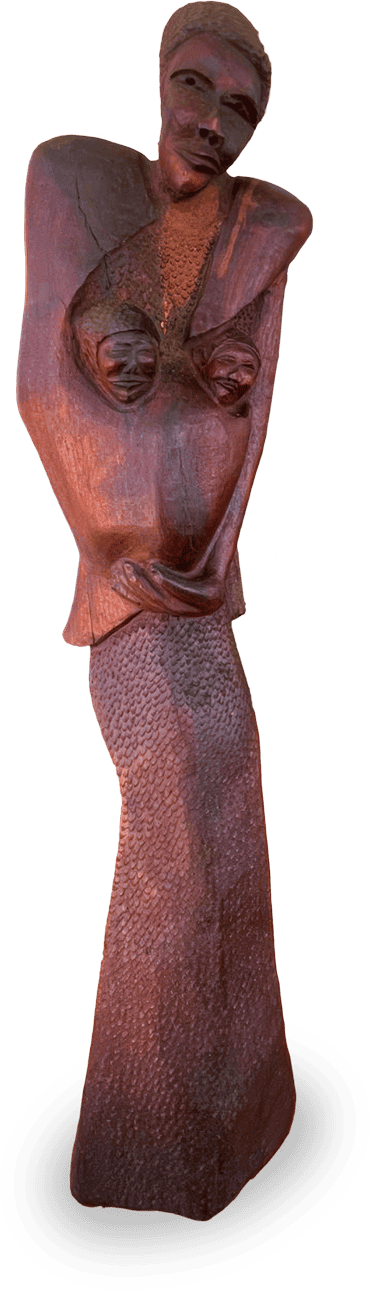 A tall, textured wooden sculpture of a woman with exaggerated, angular shoulders, prominent breasts, and arms crossed below her chest. She wears a long, close-fitting skirt, and her facial features are carved with a serene, closed-mouth expression.