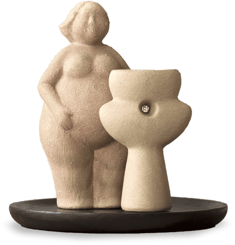 A clay figurine of a nude, full-bodied woman stands beside an abstract pedestal with a gem embedded in its centre, both positioned on a round, dark base. The figures are textured and softly coloured, emphasising curves and simplicity.