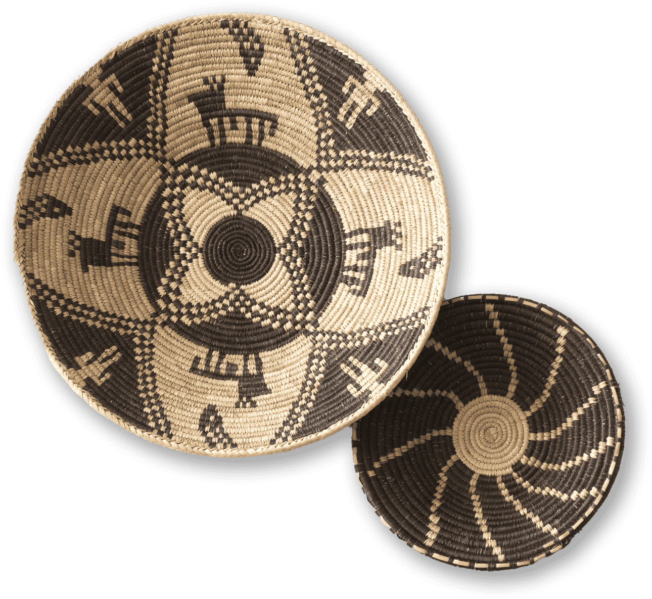 Two round, woven baskets with intricate patterns sit overlapping. The larger basket features black and cream geometric and animal designs, whilst the smaller one displays a spiralling black and cream pattern. Both have tight, detailed weaving.