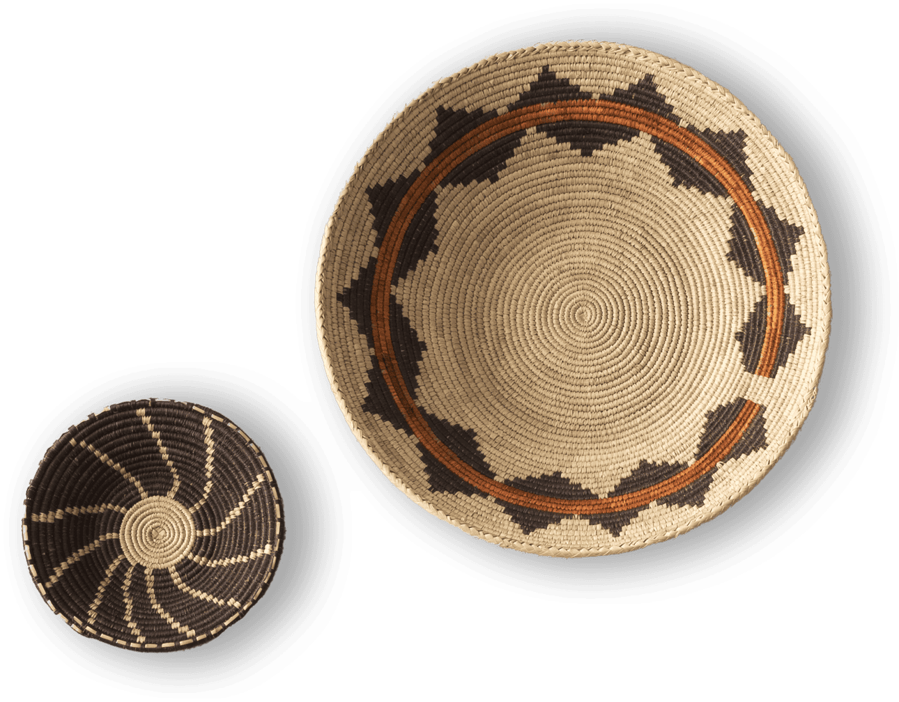Two woven baskets are displayed on a black background. The larger basket has a tan base with brown and black geometric patterns around the rim. The smaller basket is darker, featuring a black base with a spiralling tan pattern radiating from the centre.