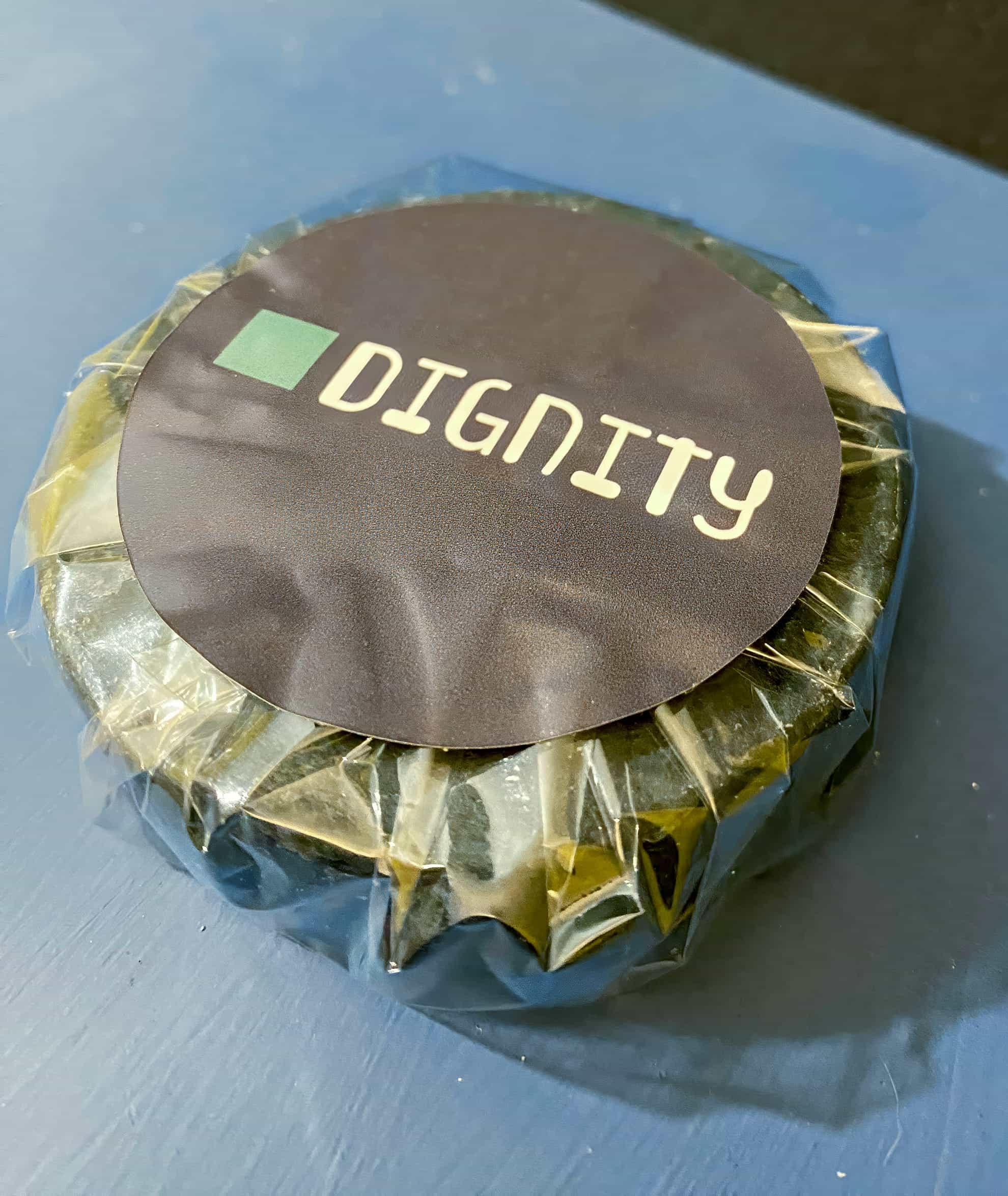 A round item wrapped in clear plastic with a black label on top displaying the word 