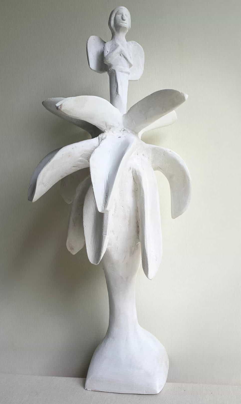 A white abstract sculpture, part of Contra.Joburg’s Weight of Silence series, features a stylised tree with thick branches and a trunk, topped by a winged human figure with outstretched arms against a pale, textured background.