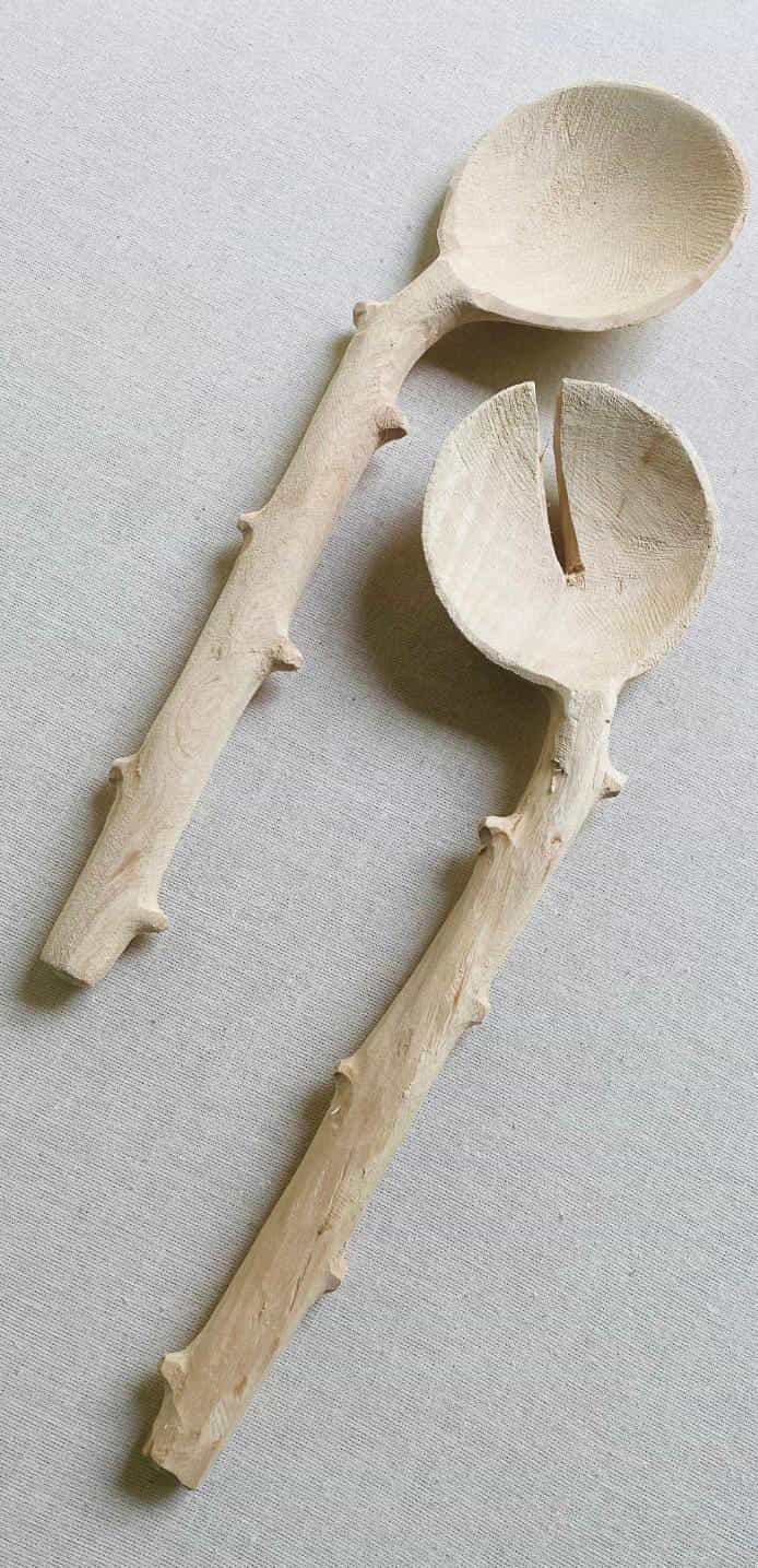 Two wooden salad servers with handles resembling natural, textured branches lay side by side on a light fabric surface—echoing the organic aesthetic found in Contra.Joburg's Weight of Silence collection.