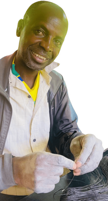 A smiling man in a jacket and yellow shirt sits against a white background, holding thin black wires in his hands. He looks directly at the camera, focused and content—a moment from the Weight of Silence series by Contra.Joburg.