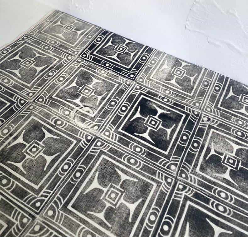 A tabletop from Contra.Joburg featuring black and white geometric tiles with a symmetrical floral and square pattern. The tiles have a slightly distressed, vintage look, and the wall behind them is textured and painted white.