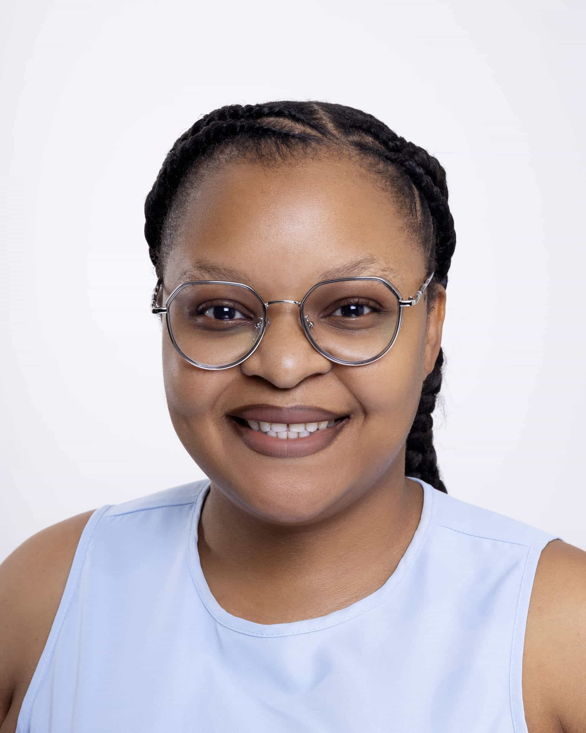 A woman with braided hair wears round glasses and a light blue sleeveless top. She is smiling and facing the camera against a plain white background.